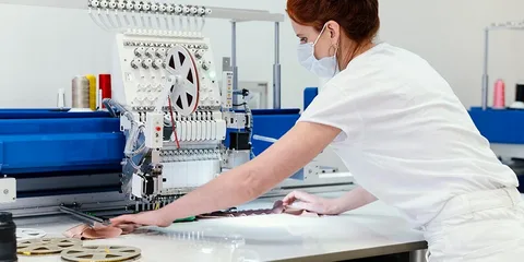 A woman in white shirt and face mask working on machine.