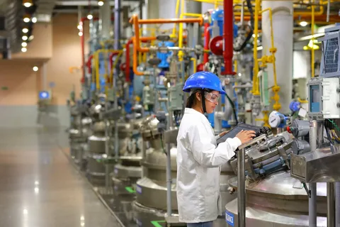 A woman in white shirt and blue helmet standing next to machinery.